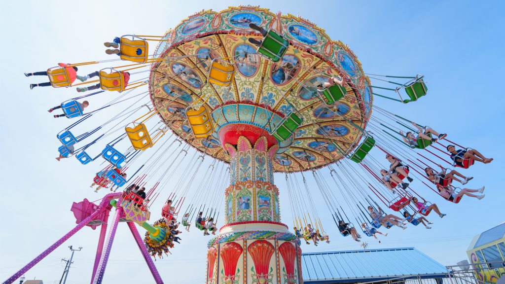A vibrant swing carousel ride with riders swinging mid-air against a blue sky.